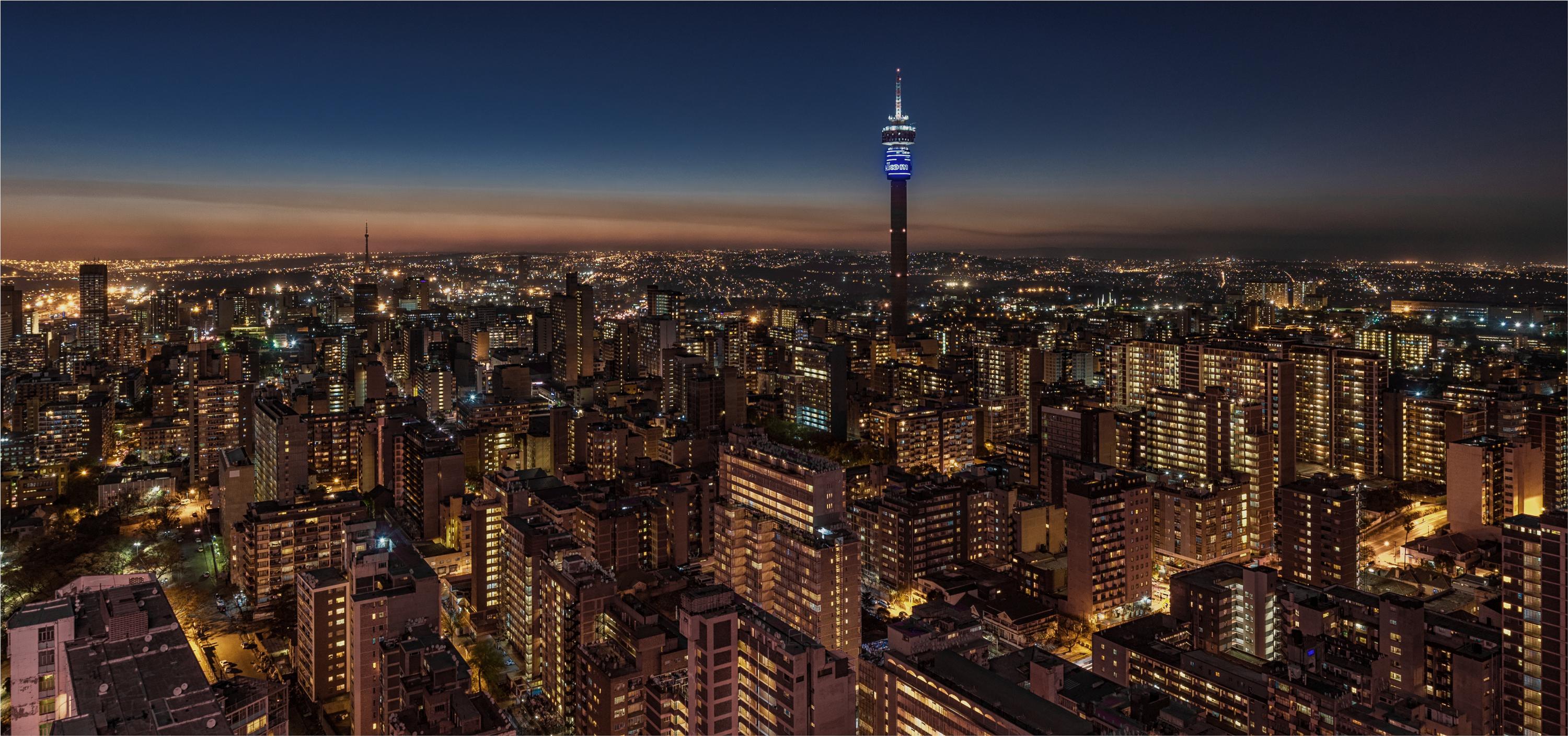 A cityscape view of Johannesburg at dusk, showcasing the city's skyline with brightly lit buildings.