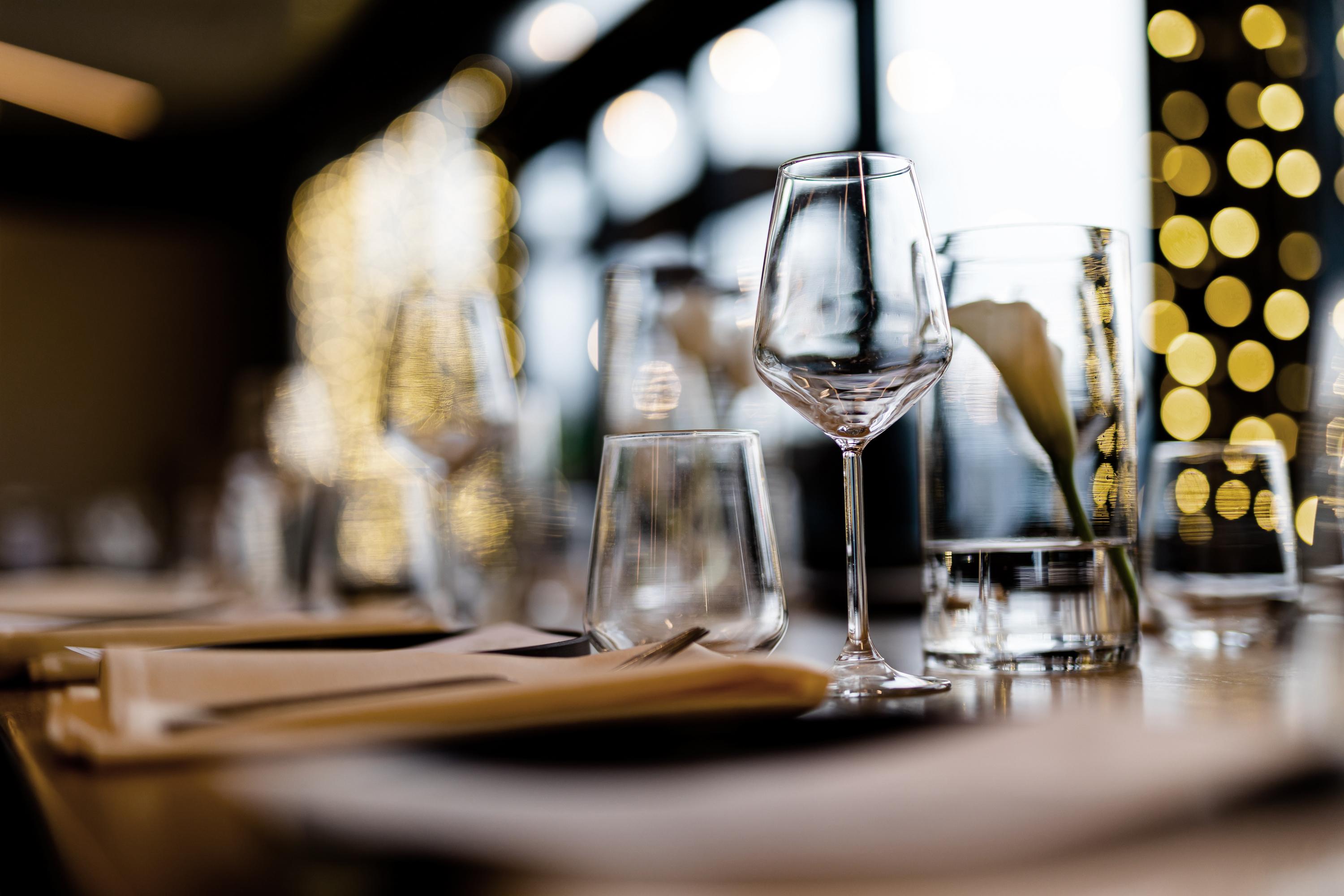 Elegant, formal dining setup with wine glasses, cutlery, and tablecloths in a dimly lit restaurant. 