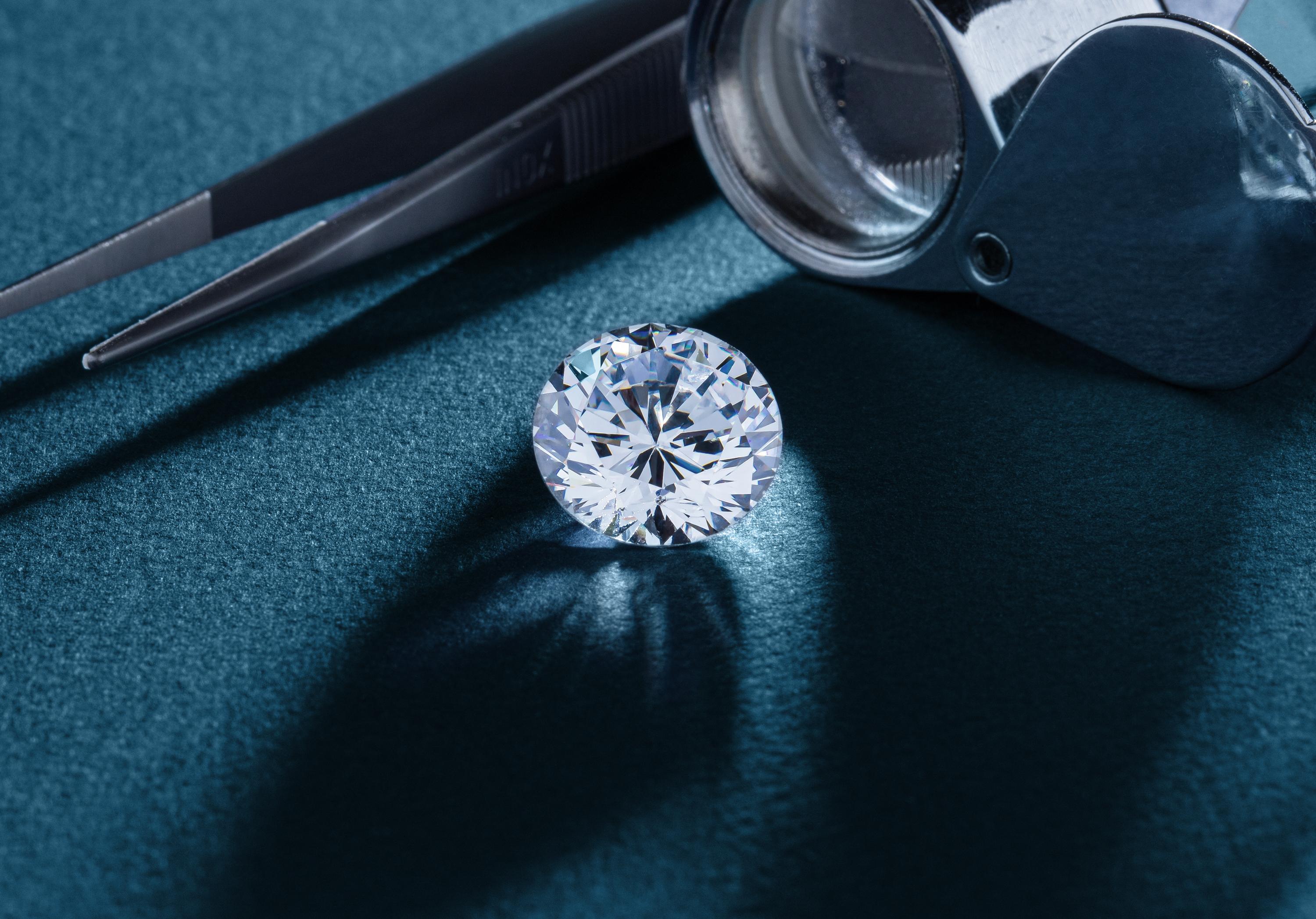 Close-up shot of a sparkling diamond being inspected with a magnifying loupe, with a diamond tweezer nearby. 