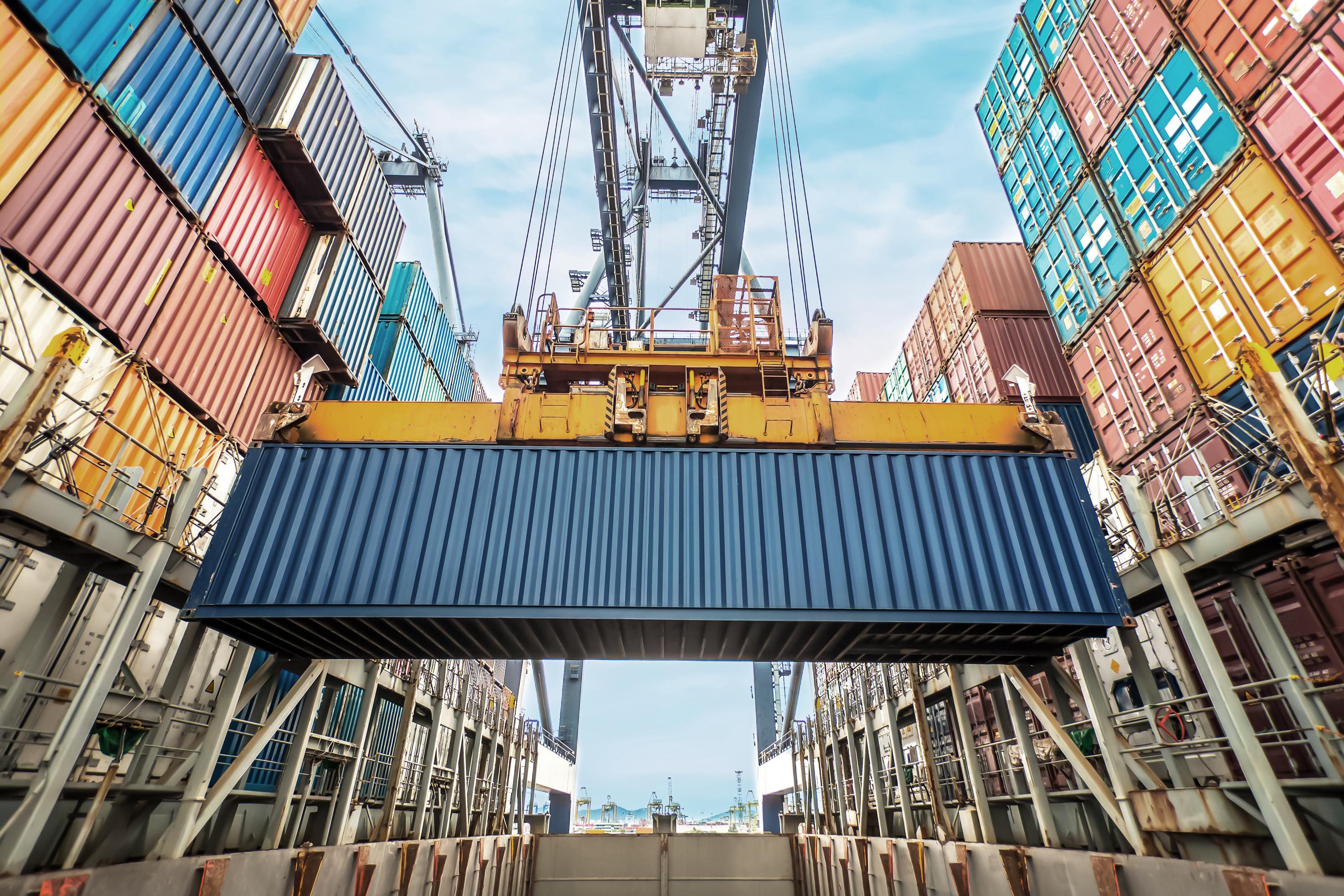 A black shipping container being lifted by a crane in a busy port.