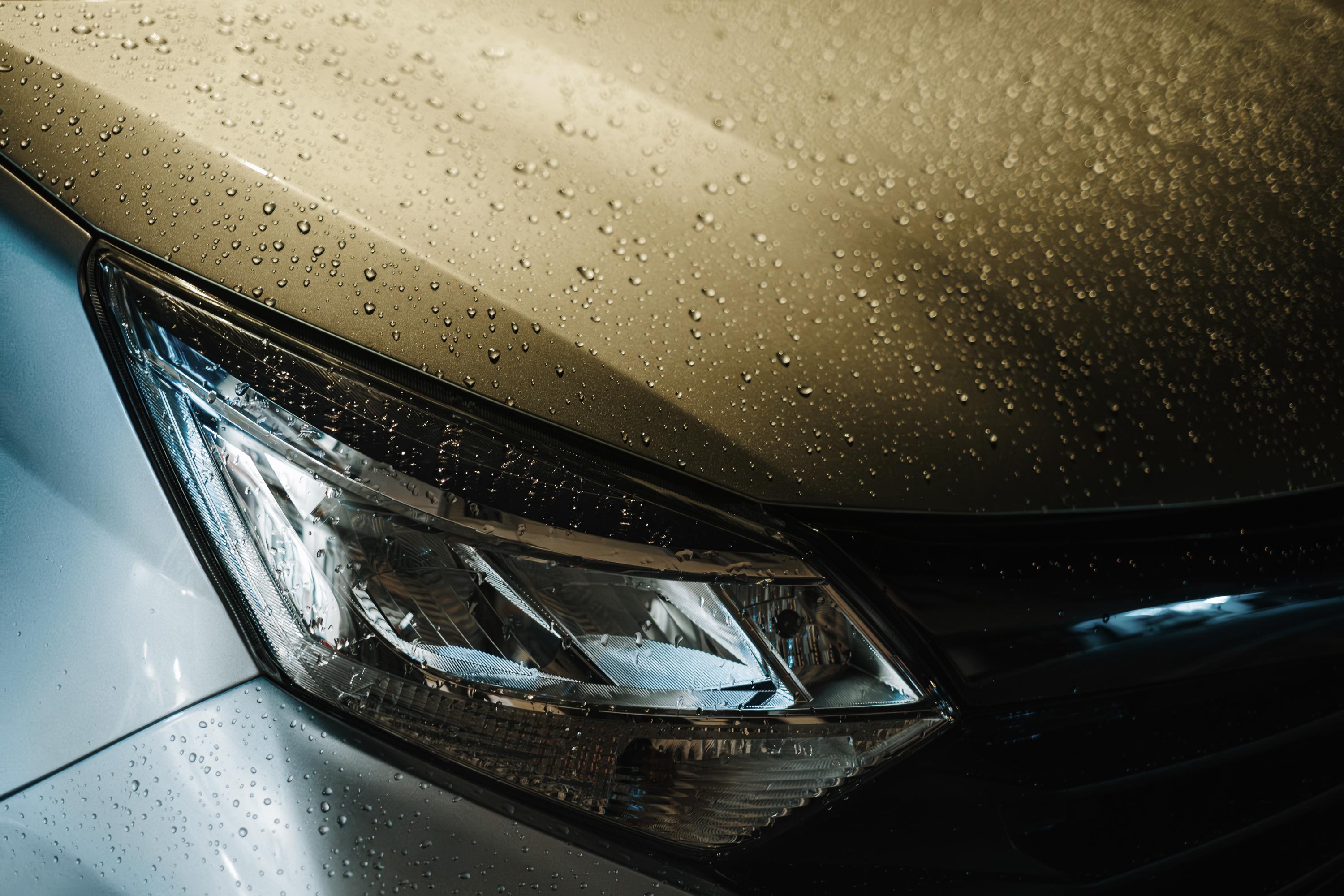 A close-up of a car’s sleek headlight and bonnet covered in rain droplets.