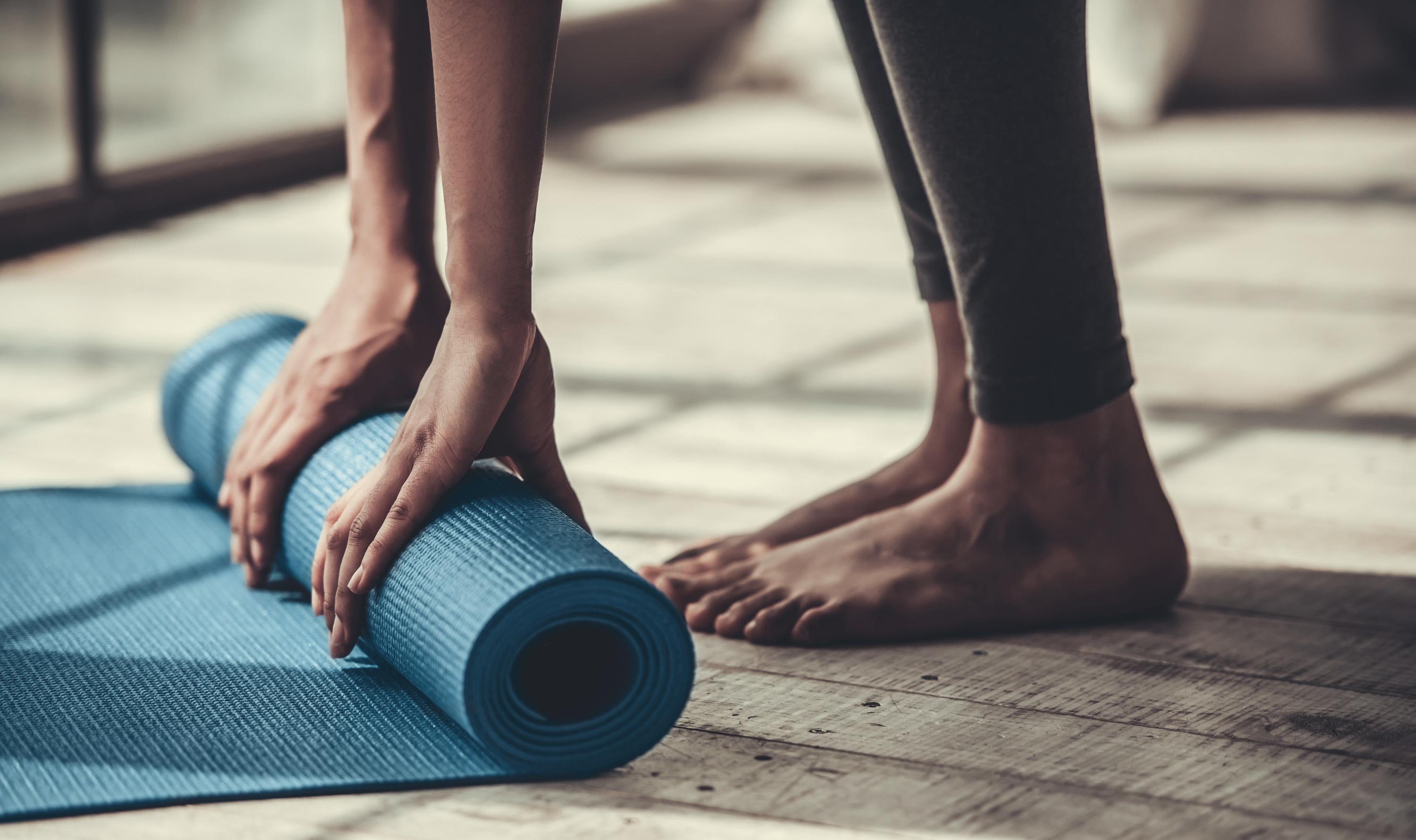 A person rolling up a blue yoga mat, with bare feet visible. 