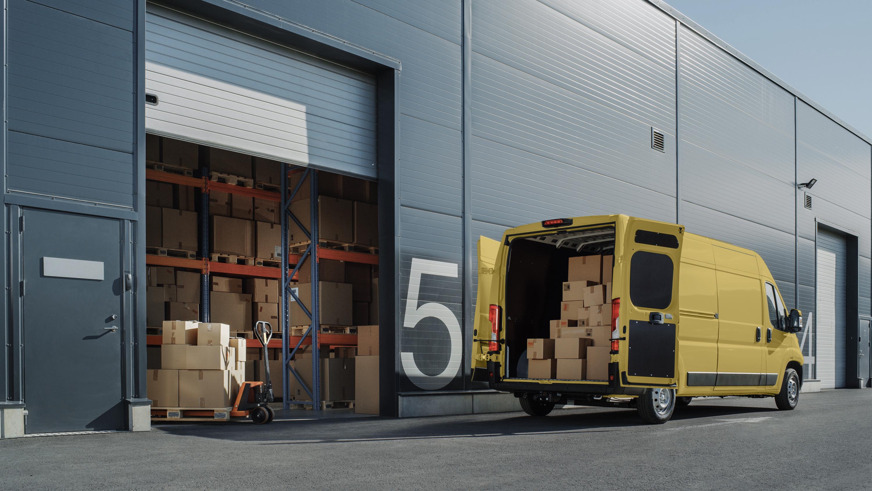 A commercial warehouse loading dock with a yellow delivery van backed into the bay.