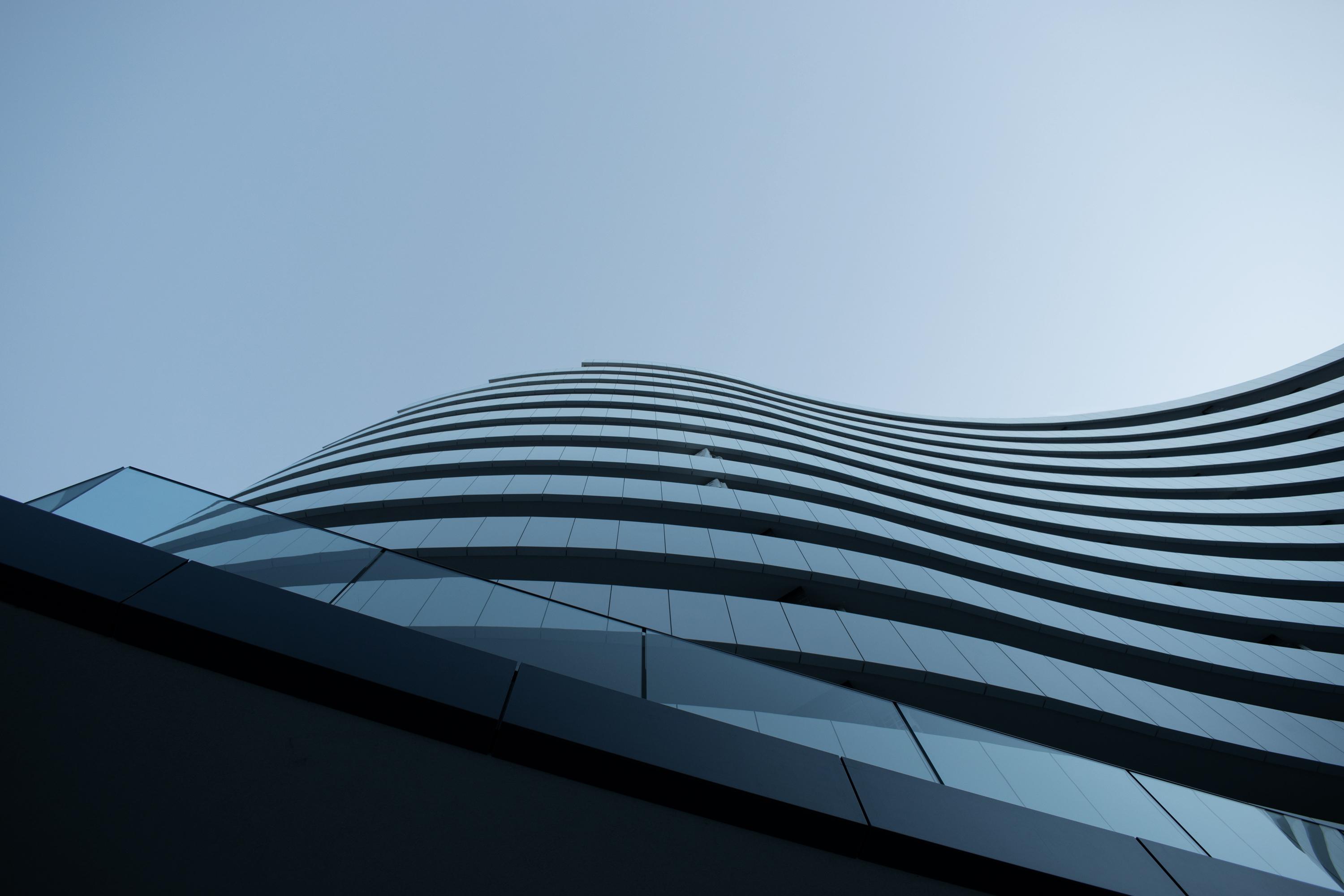 A modern, sleek corporate building with white wave-like architectural lines against a clear blue sky.